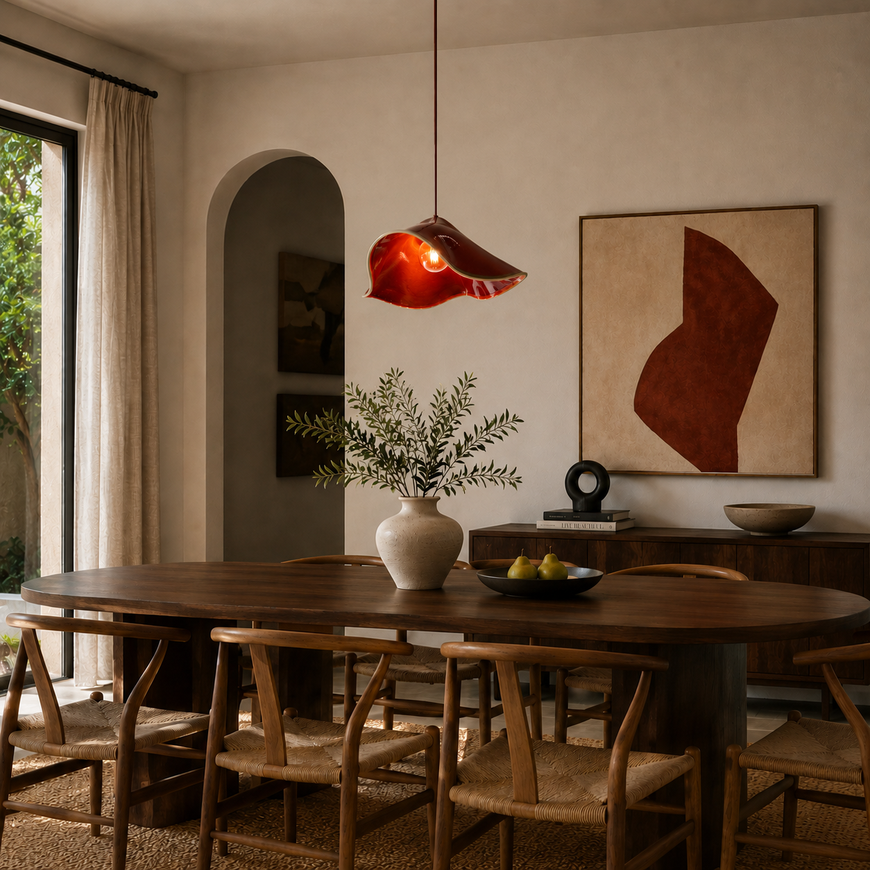 Handcrafted sculptural ceramic pendant light in a glossy shiraz red finish centred above a contemporary timber dining table in a warm minimalist interior with natural textures, curved architecture and Mediterranean-inspired styling.