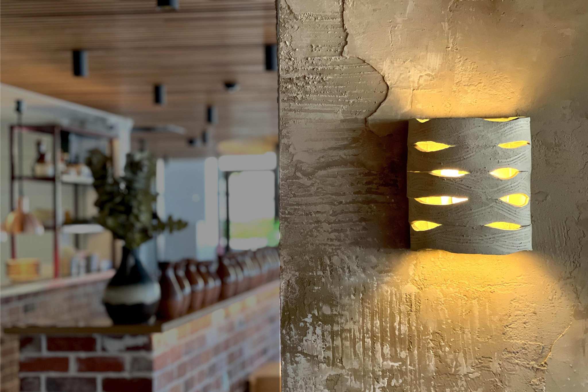 Handcrafted ceramic wall sconce creating warm ambient light in restaurant interior by Carver Lights Australia