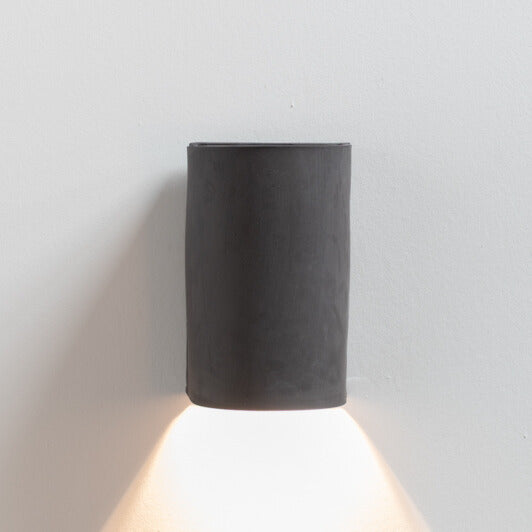Charcoal Wall Sconce handcrafted ceramic wall light Australia made from raw unglazed black clay lit showing warm ambient light cast downward