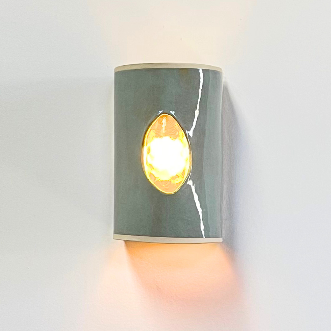 Eucalyptus ceramic wall sconce with textured glass illuminated with a warm glow.
