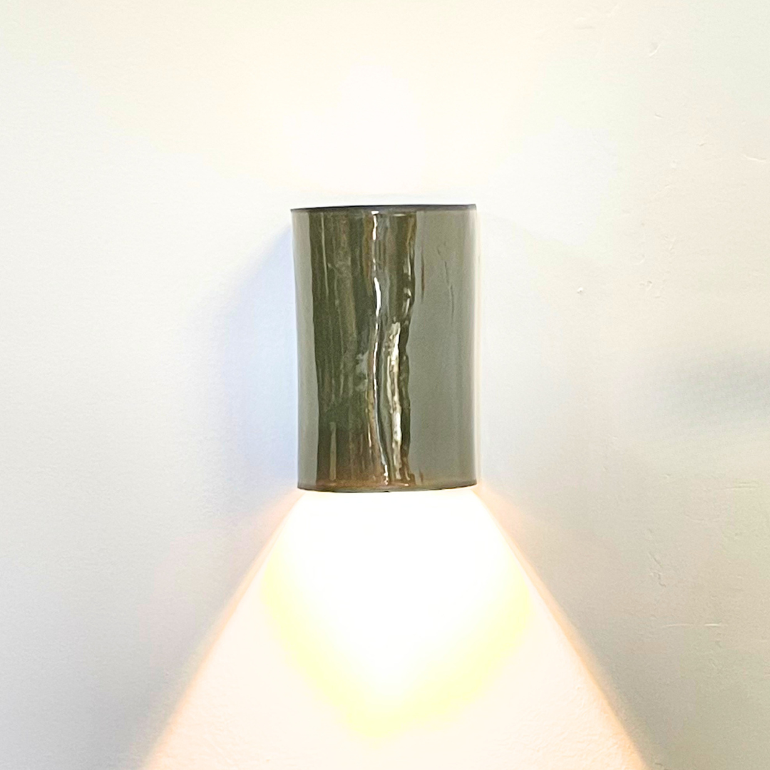Olive glazed handmade ceramic wall light casting a warm downward glow.