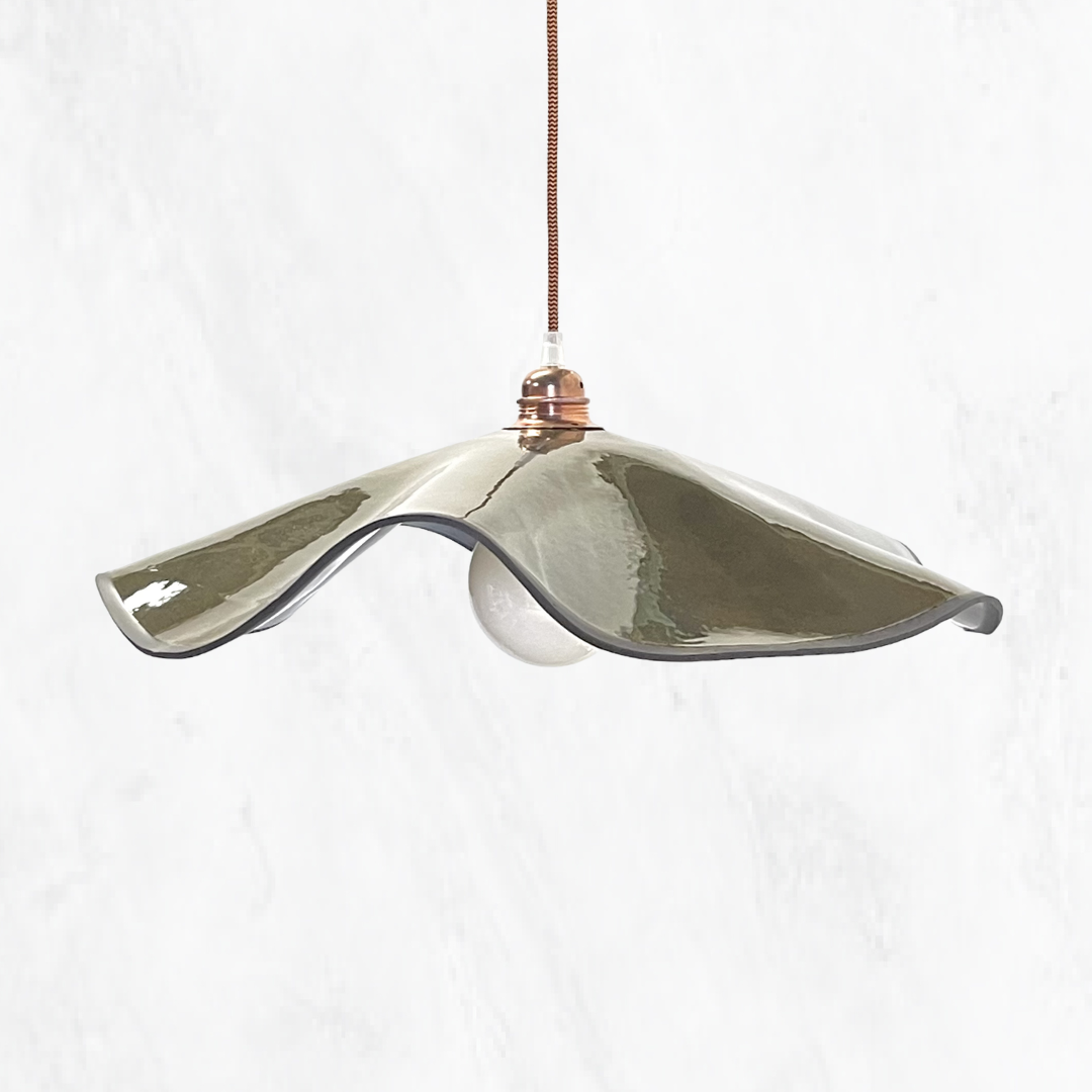 Olive Marilyn handmade ceramic pendant light with a flowing sculptural ceramic shade, glossy olive glaze, white globe and warm copper suspension, shown against a light textured background.