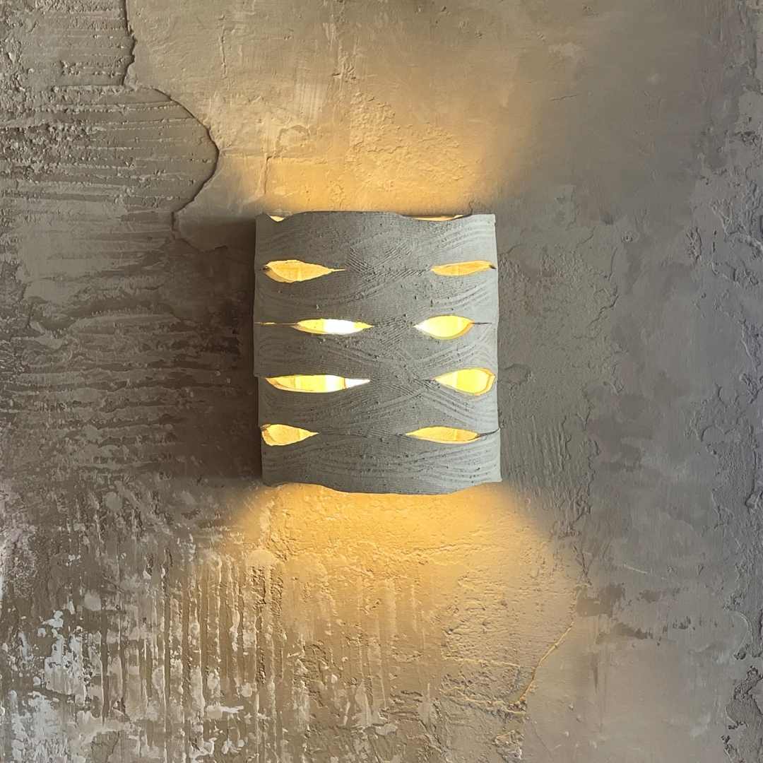 Rune ceramic wall sconce mounted on a textured plaster wall, casting warm ambient light through carved openings above and below.