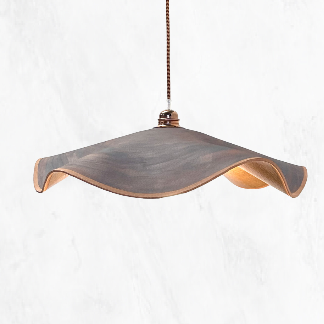 Rust Marilyn handmade ceramic pendant light with a flowing sculptural ceramic shade, raw rust finish, warm illuminated interior and copper suspension, shown against a light textured background.