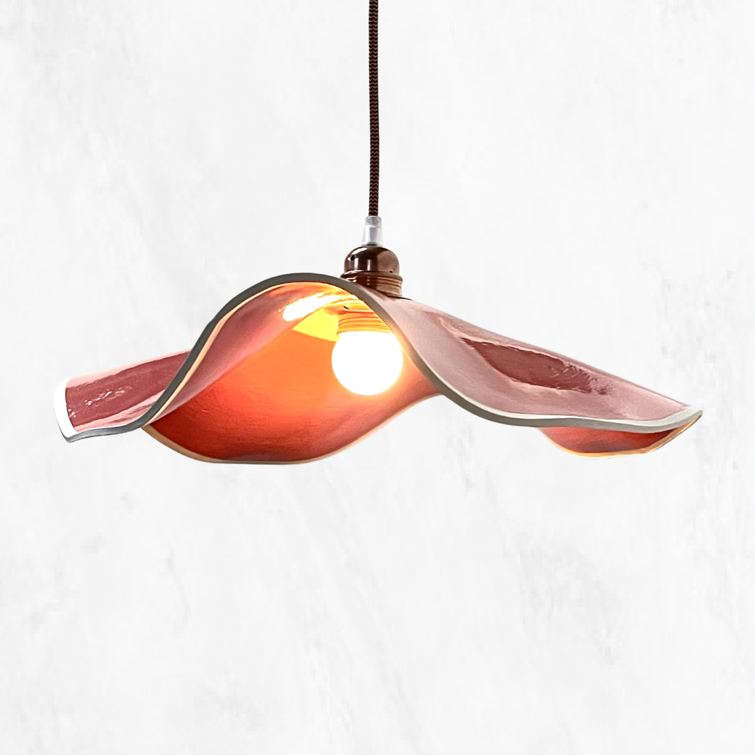 Salmon Marilyn handmade ceramic pendant light with a flowing sculptural ceramic shade, glossy salmon glaze, warm illuminated interior and copper suspension, shown against a light textured background.