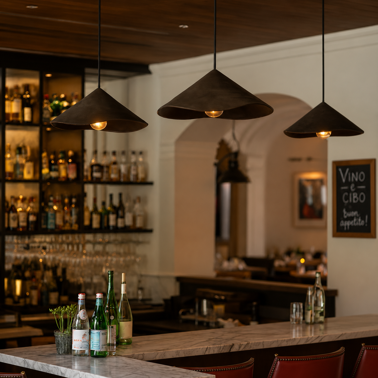 Three handcrafted sculptural ceramic pendant lights in a matte charcoal-black finish hanging above a marble bar in a warm contemporary restaurant interior with timber ceilings, ambient lighting, wine shelving and rich textured materials.