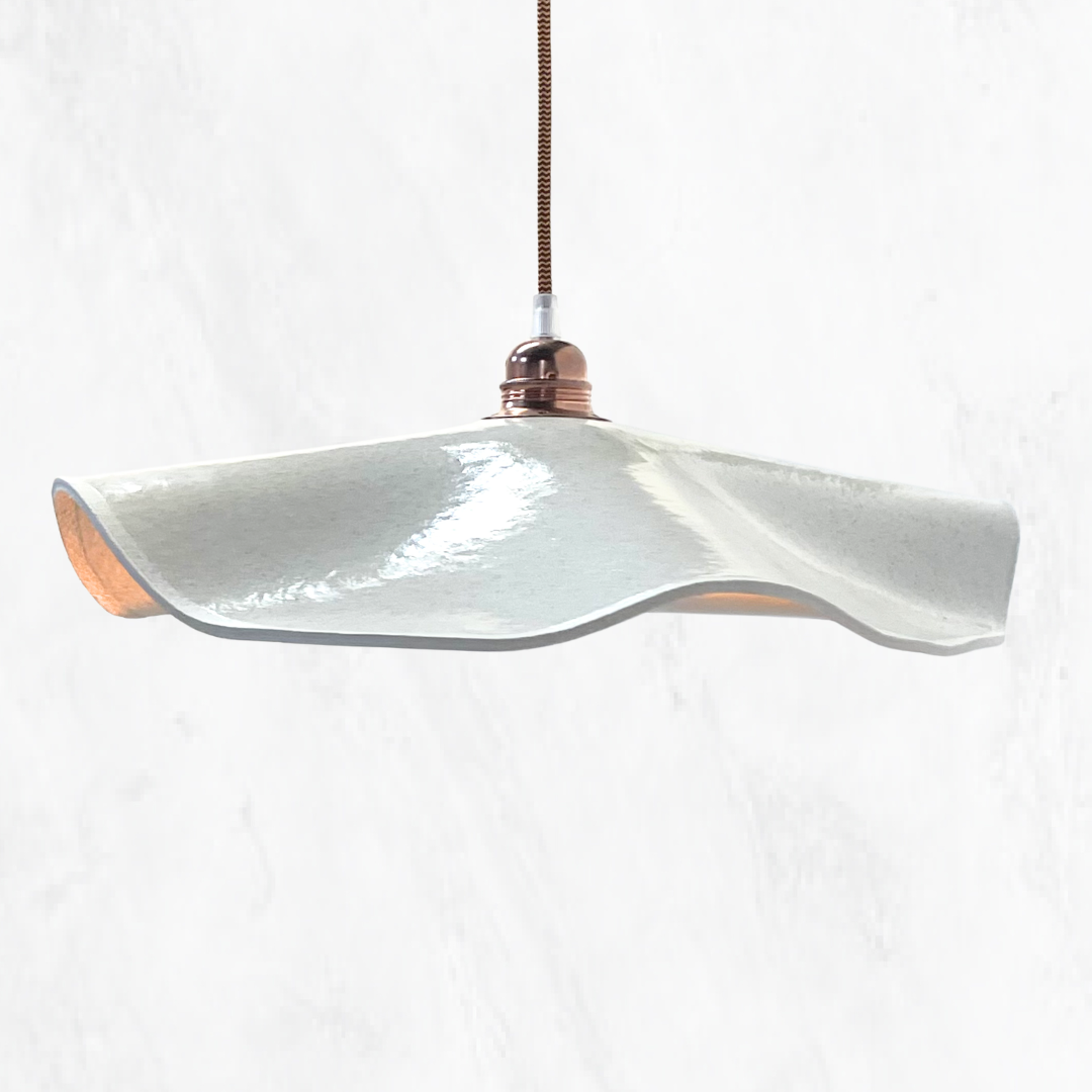 Stone Marilyn handmade ceramic pendant light with a flowing sculptural ceramic shade, glossy stone glaze and warm copper suspension, shown against a light textured background.