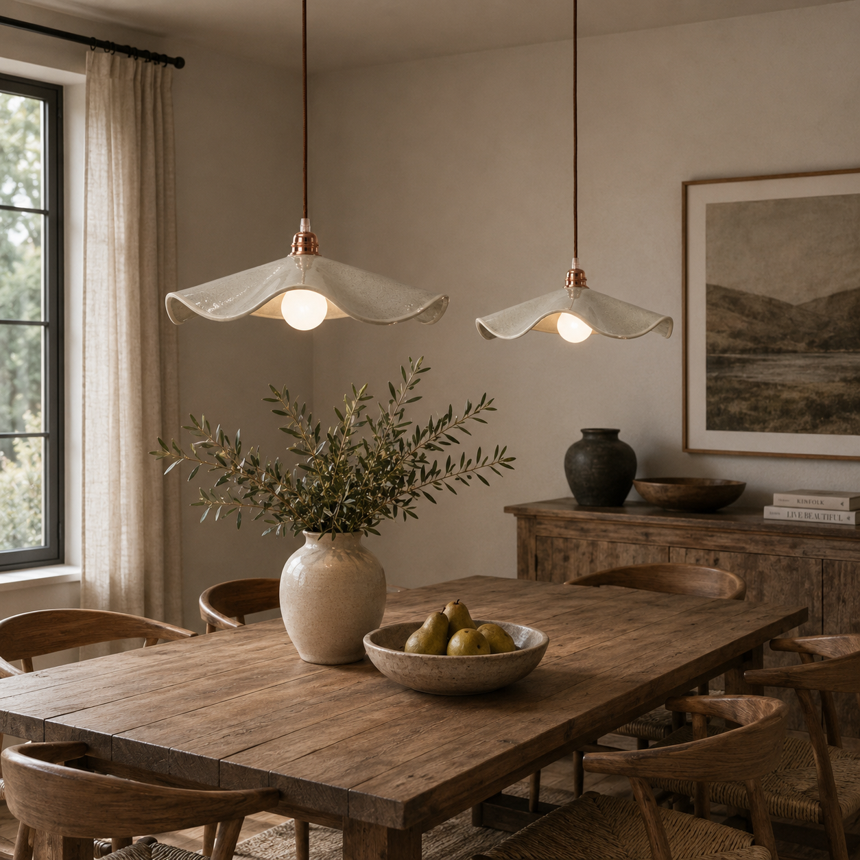 Two Stone Marilyn handmade ceramic pendant lights hanging at different heights above a solid timber dining table in a modern dining room, creating a soft warm ambient glow.

